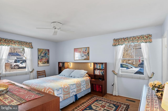 bedroom with baseboards, ceiling fan, visible vents, and wood finished floors