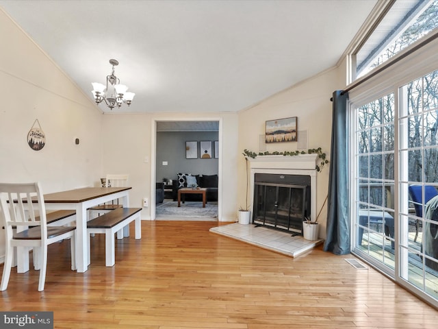 dining space featuring visible vents, a tiled fireplace, lofted ceiling, light wood-style floors, and a notable chandelier