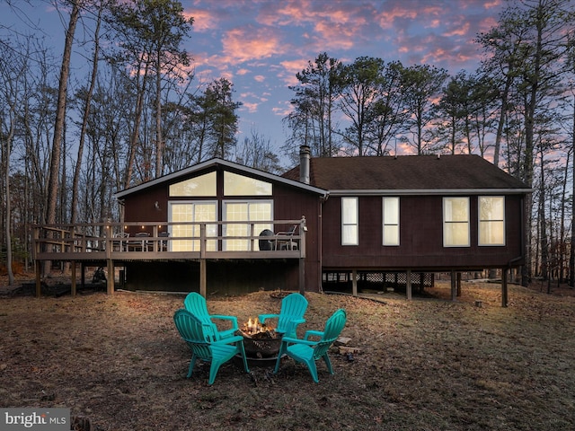 back of house at dusk featuring an outdoor fire pit, roof with shingles, and a wooden deck