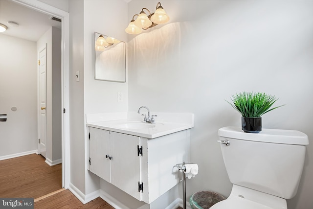 bathroom with toilet, wood finished floors, visible vents, vanity, and baseboards