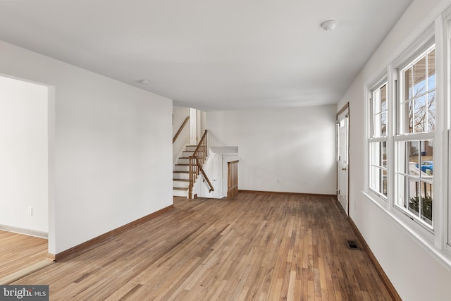 empty room with light wood-type flooring, baseboards, stairs, and visible vents