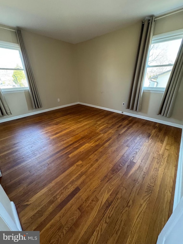 empty room with dark wood-type flooring, a healthy amount of sunlight, and baseboards