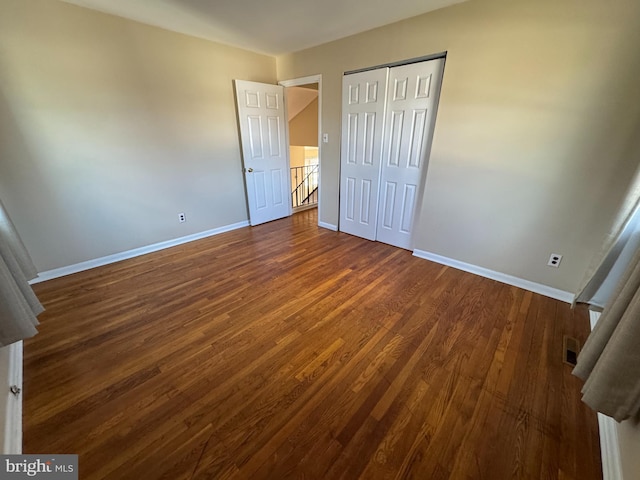 unfurnished bedroom with dark wood-type flooring, a closet, visible vents, and baseboards