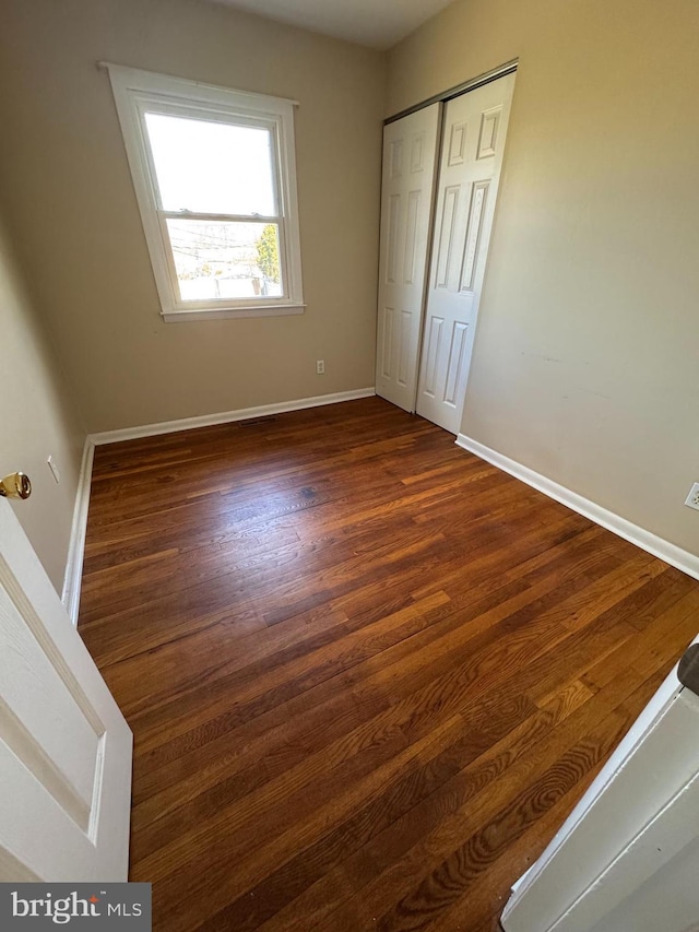 unfurnished bedroom with dark wood-style floors, a closet, and baseboards