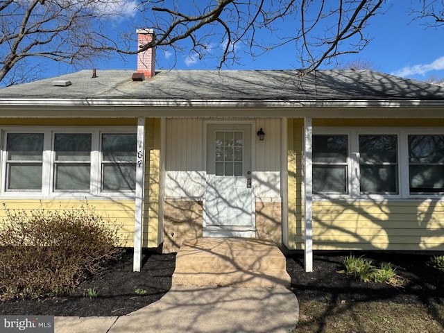 doorway to property with roof with shingles and a chimney