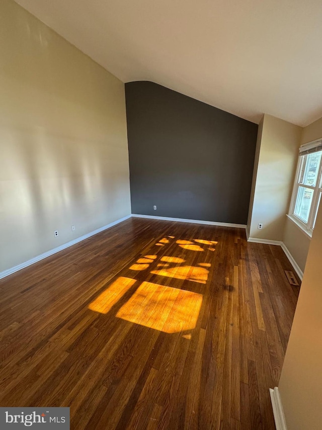 spare room featuring lofted ceiling, baseboards, visible vents, and dark wood finished floors