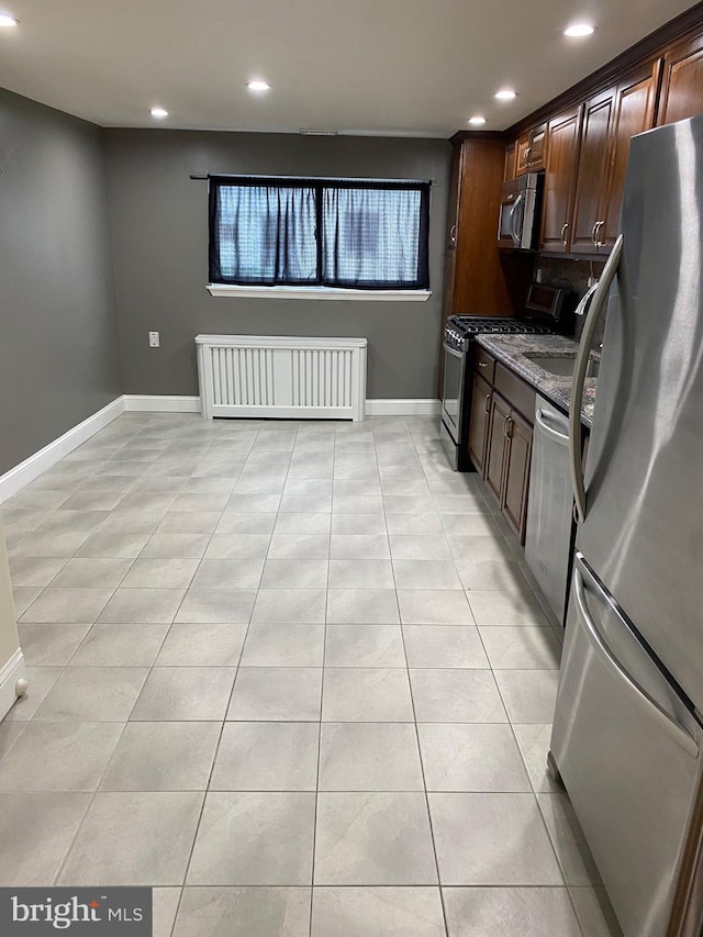 kitchen with appliances with stainless steel finishes, radiator heating unit, light tile patterned floors, and dark stone countertops