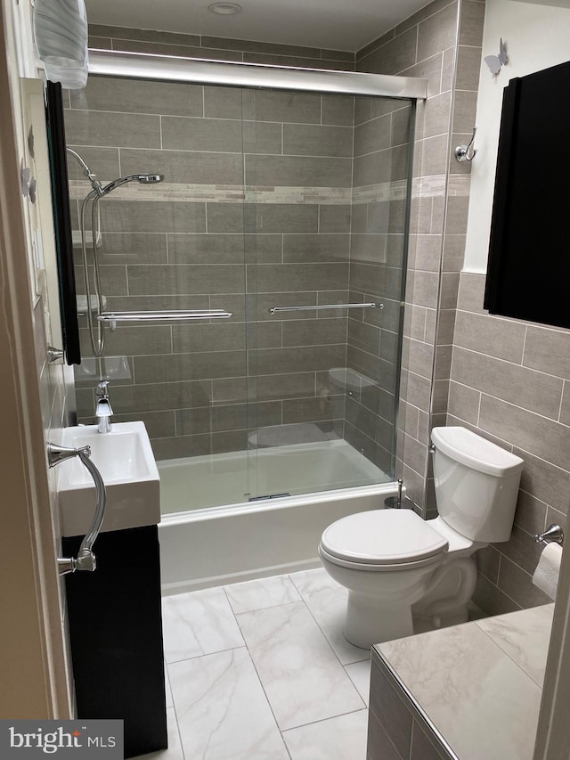 full bathroom featuring shower / bath combination with glass door, vanity, toilet, and tile walls