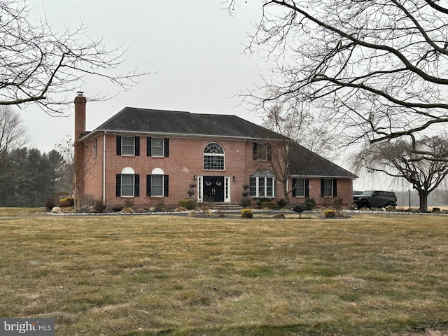 view of front of house featuring brick siding, a chimney, and a front yard