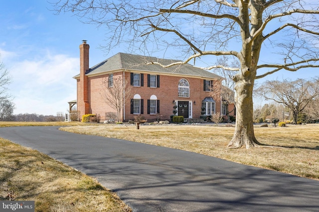 georgian-style home with a chimney, a front lawn, and brick siding