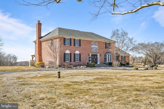 colonial-style house featuring brick siding, a chimney, and a front lawn