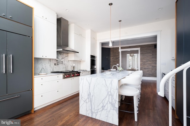 kitchen featuring white cabinetry, wall chimney exhaust hood, dark wood-style flooring, and appliances with stainless steel finishes