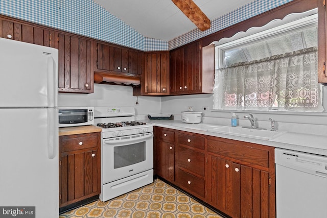 kitchen with a sink, white appliances, under cabinet range hood, light countertops, and wallpapered walls