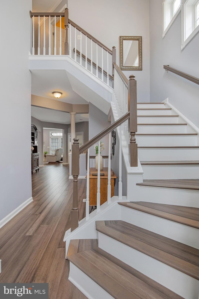 staircase with wood finished floors, a towering ceiling, and baseboards