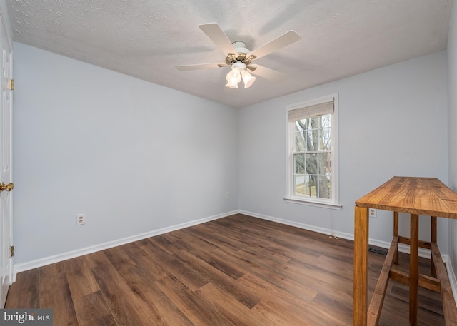 empty room featuring a textured ceiling, wood finished floors, a ceiling fan, and baseboards