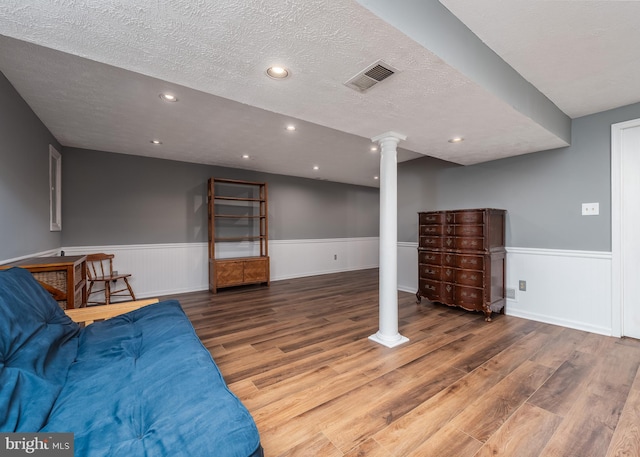 interior space with decorative columns, visible vents, wainscoting, a textured ceiling, and wood finished floors