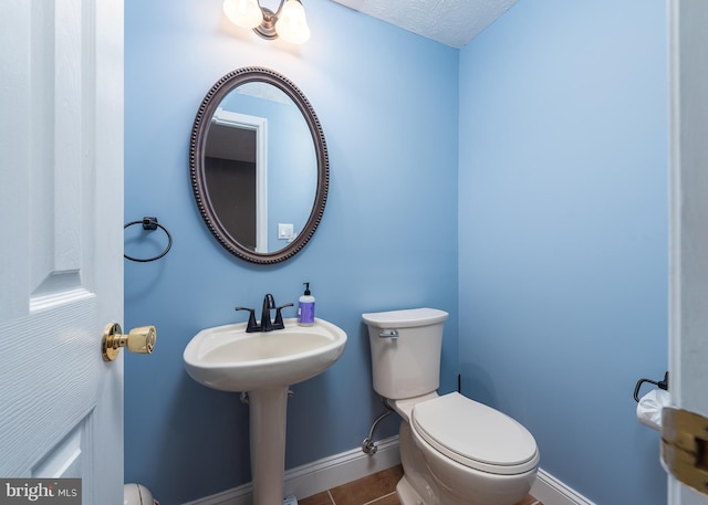 half bath featuring toilet, tile patterned flooring, baseboards, and a textured ceiling