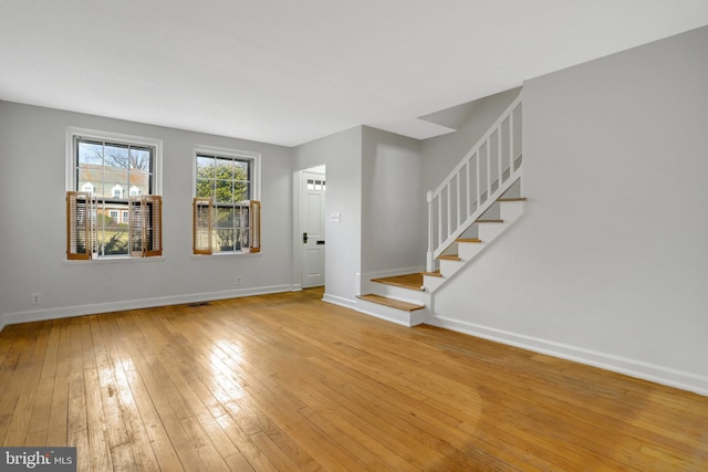 unfurnished room featuring light wood finished floors, baseboards, visible vents, and stairway