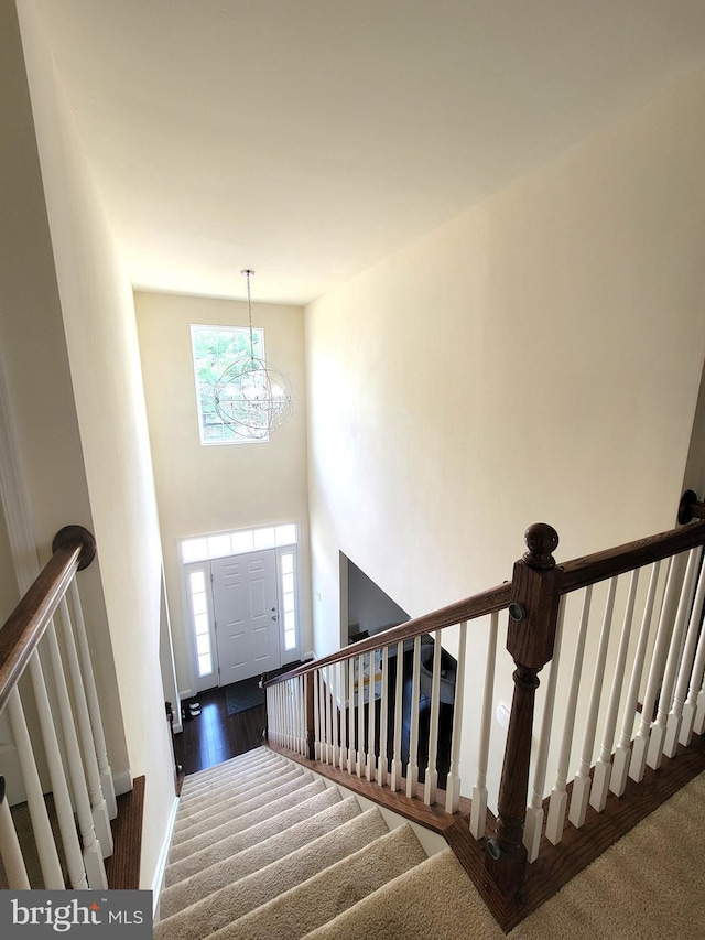 stairway with hardwood / wood-style flooring, a towering ceiling, and a chandelier