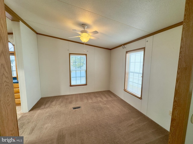 empty room with a textured ceiling, ornamental molding, carpet, and visible vents