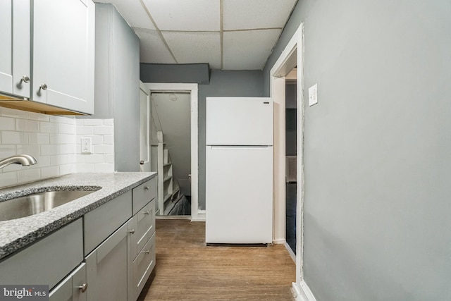 kitchen featuring a paneled ceiling, tasteful backsplash, sink, white fridge, and light hardwood / wood-style flooring