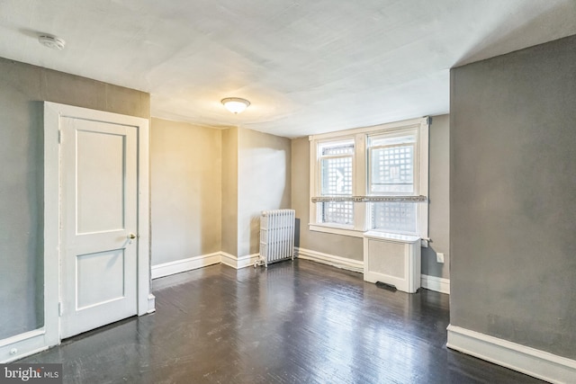 unfurnished room featuring radiator heating unit and dark hardwood / wood-style floors