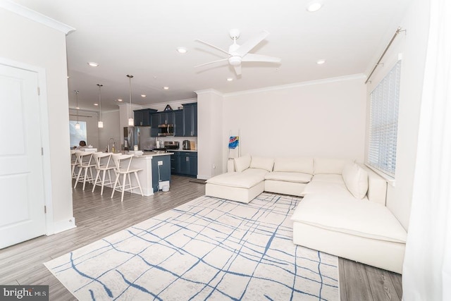 living area with light wood-style floors, ceiling fan, ornamental molding, and recessed lighting