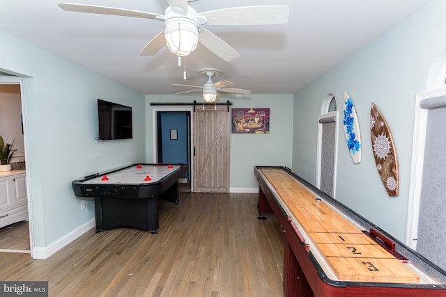 game room with a barn door, baseboards, light wood-style flooring, and a ceiling fan