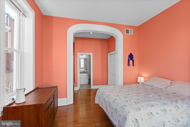 bedroom with arched walkways, dark wood finished floors, visible vents, and baseboards