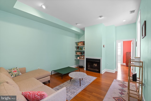 living room featuring a warm lit fireplace, recessed lighting, wood finished floors, visible vents, and baseboards