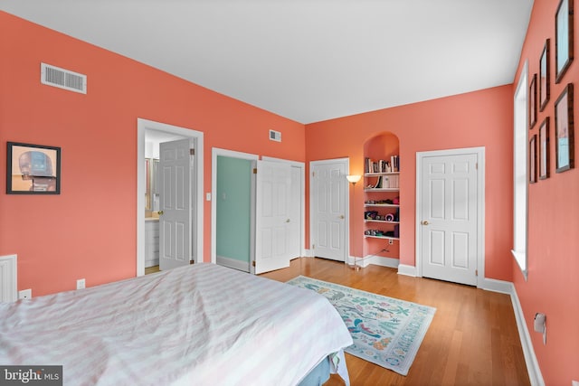 bedroom with baseboards, wood finished floors, visible vents, and multiple closets