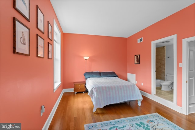 bedroom featuring visible vents, ensuite bath, baseboards, and wood finished floors