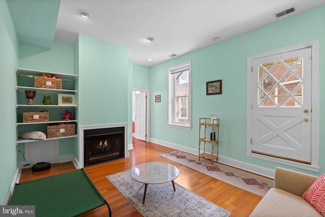 living room with a warm lit fireplace, visible vents, and wood finished floors