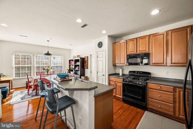 kitchen with sink, decorative light fixtures, dark wood-type flooring, black appliances, and a kitchen island with sink