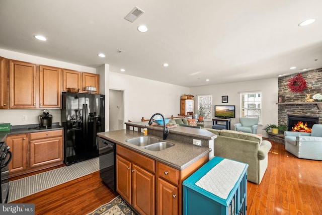 kitchen with light wood-type flooring, an island with sink, black appliances, a fireplace, and sink