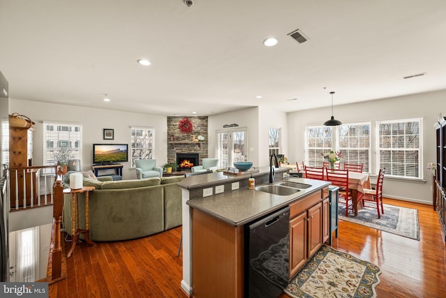 kitchen featuring a center island with sink, sink, dishwasher, dark hardwood / wood-style flooring, and a fireplace