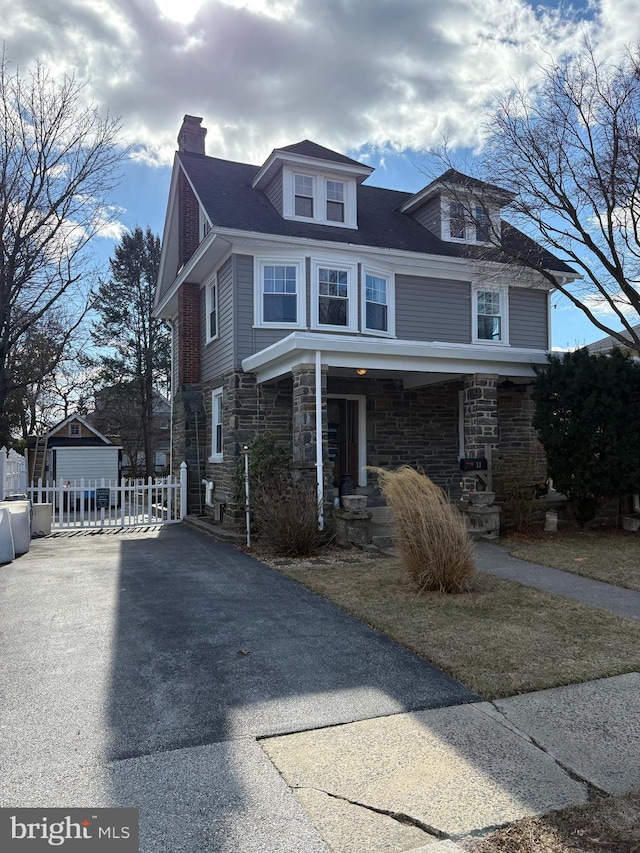 american foursquare style home with stone siding, an outdoor structure, and a chimney