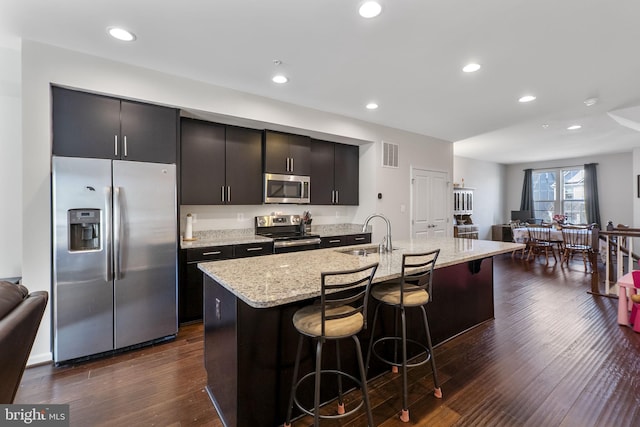 kitchen with visible vents, a breakfast bar, a kitchen island with sink, stainless steel appliances, and a sink