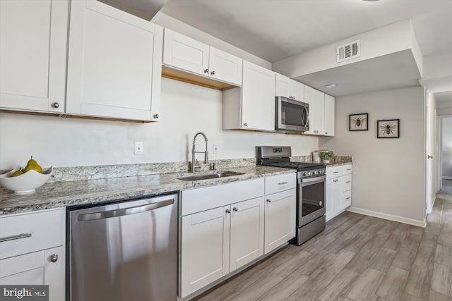 kitchen featuring visible vents, white cabinets, appliances with stainless steel finishes, light stone countertops, and a sink