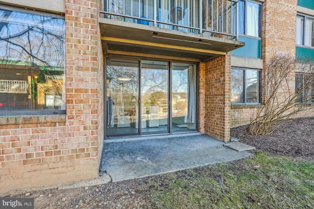 view of exterior entry featuring a balcony and brick siding