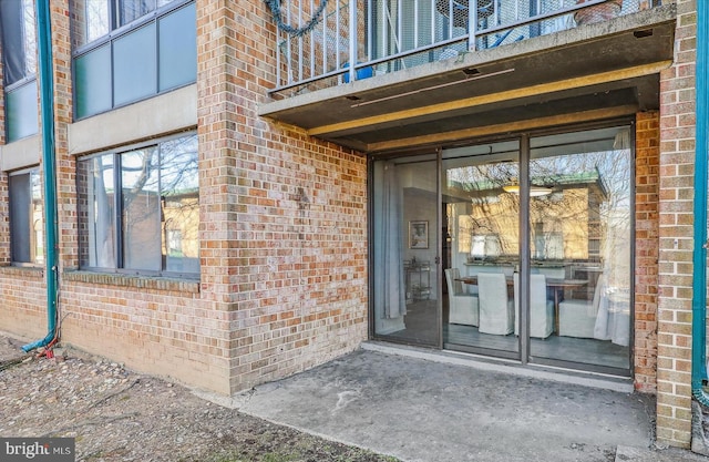 view of exterior entry with brick siding and a balcony