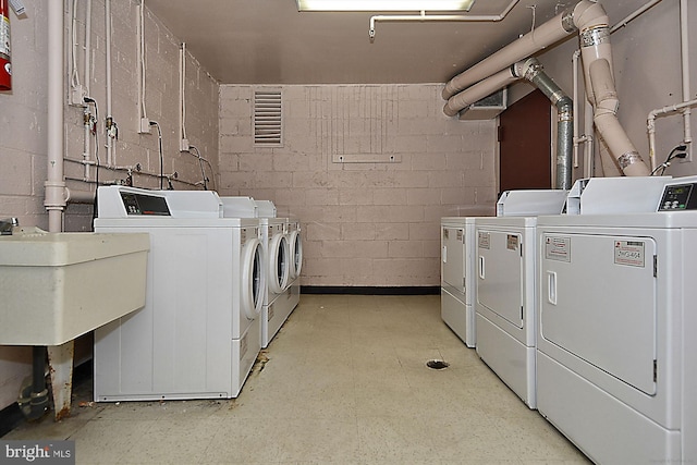 washroom featuring concrete block wall, light floors, a sink, and washing machine and clothes dryer