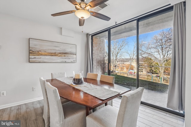 dining area with a ceiling fan, baseboards, a wall of windows, and wood finished floors