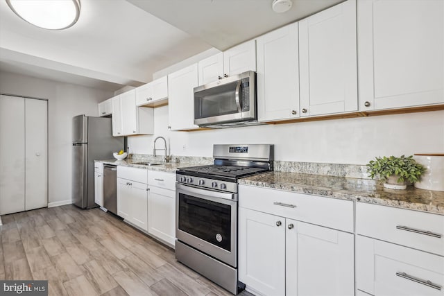 kitchen featuring light stone counters, stainless steel appliances, light wood-style flooring, white cabinetry, and a sink