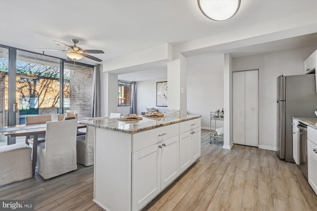 kitchen featuring light stone counters, floor to ceiling windows, light wood-style floors, appliances with stainless steel finishes, and white cabinetry