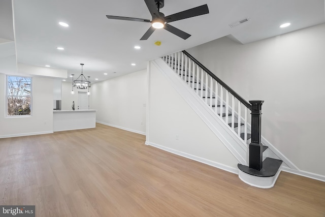 unfurnished living room with sink, ceiling fan with notable chandelier, and light hardwood / wood-style floors