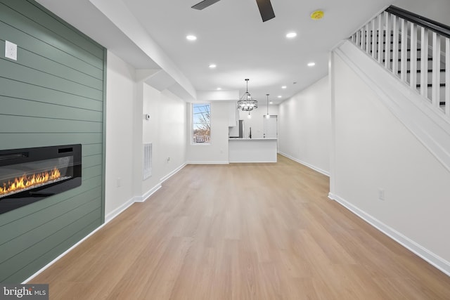 unfurnished living room with ceiling fan with notable chandelier and light hardwood / wood-style floors