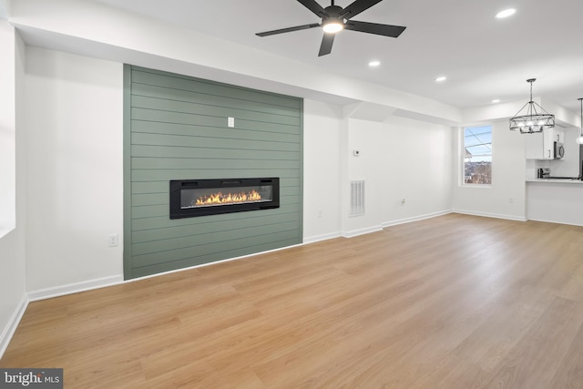 unfurnished living room featuring ceiling fan with notable chandelier, a large fireplace, and light wood-type flooring