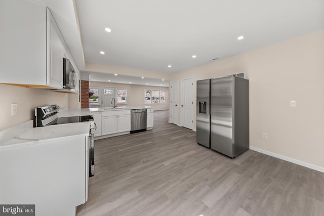 kitchen with a peninsula, a sink, stainless steel appliances, white cabinets, and light wood-style floors