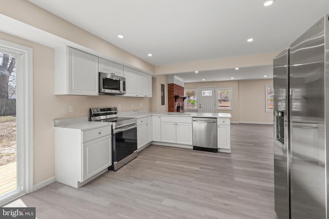 kitchen featuring a peninsula, a sink, light countertops, appliances with stainless steel finishes, and white cabinetry